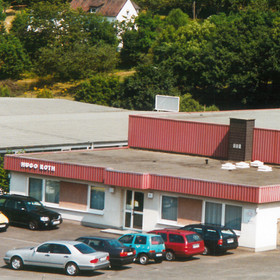 Foto auf Entfernung auf das Gebäude von 1982 in Wilnsdorf, auf dem Parkplatz stehen Autos